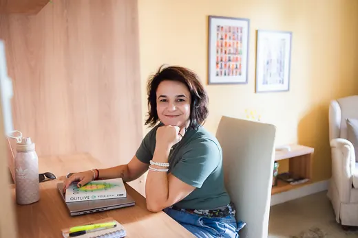 Melissa em sua mesa de estudos, sorrindo, com livros sobre saúde