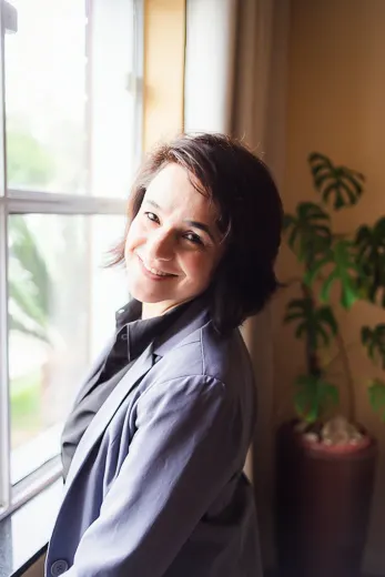 Melissa Teixeira sorrindo ao lado da janela do consultório, com luz natural